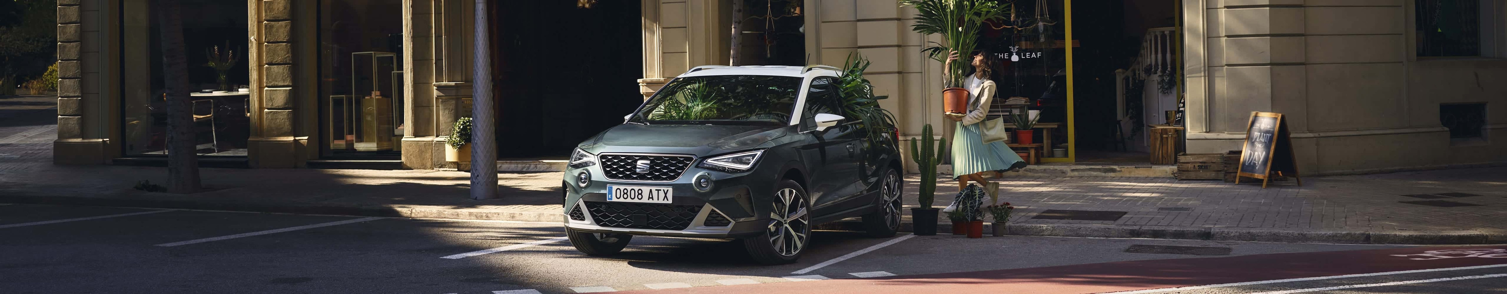 Woman with a plant walking to SEAT arona dark camouflage colour