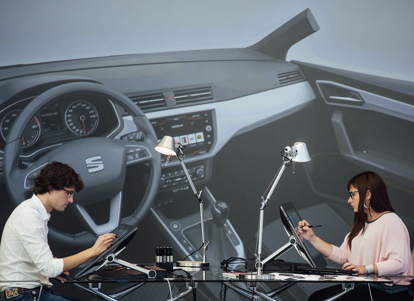 Two new car designers drawing on electronic display units with a photo backdrop of the interior of a car – SEAT Human Resources