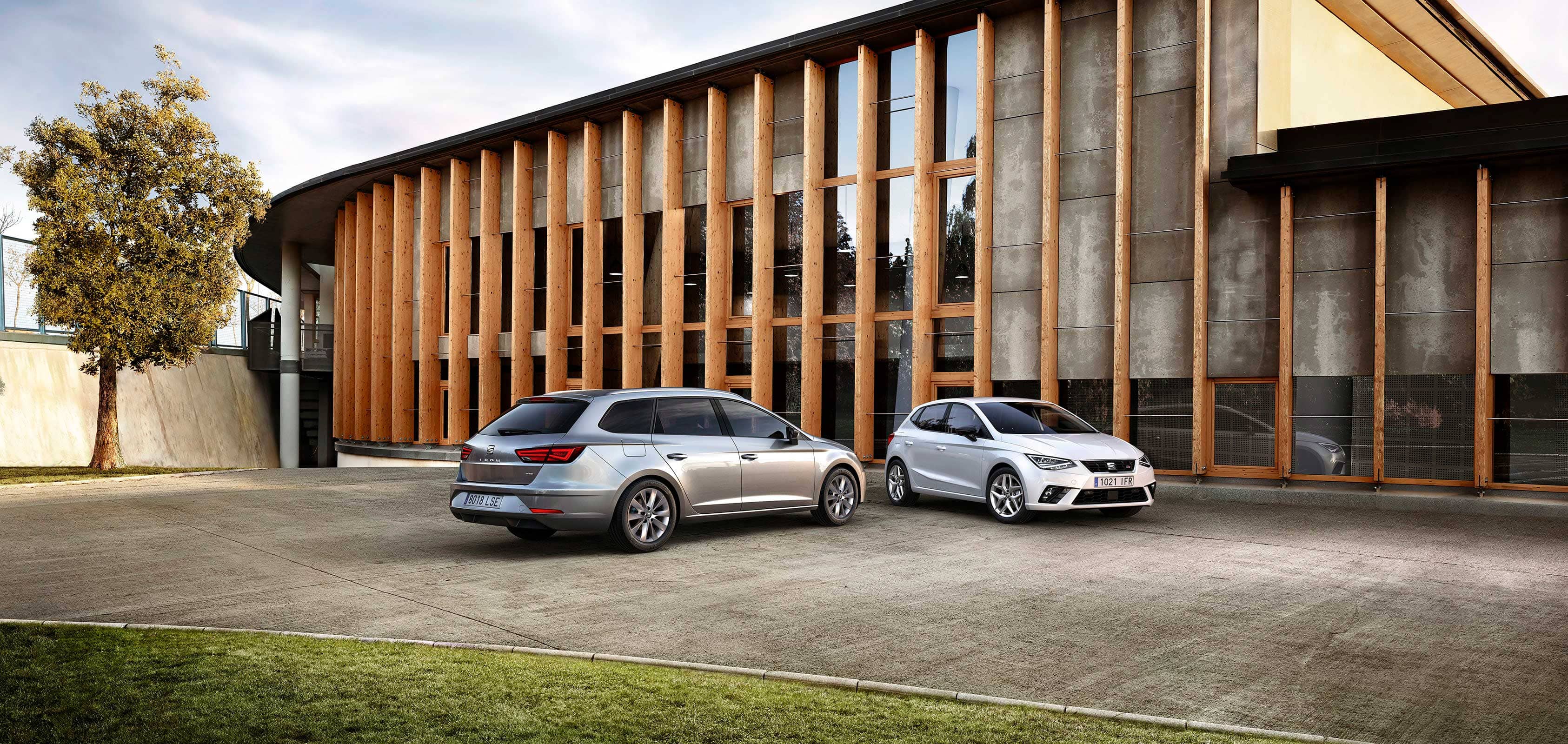 Two cars parked in front of a building with wooden panels – SEAT For Business fleet services.