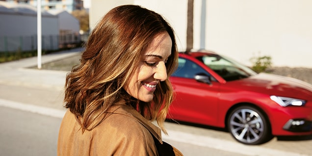 rear view of a red leon 5d,parked in an open parking space and a woman, as main object of the photo, leaning on a pole