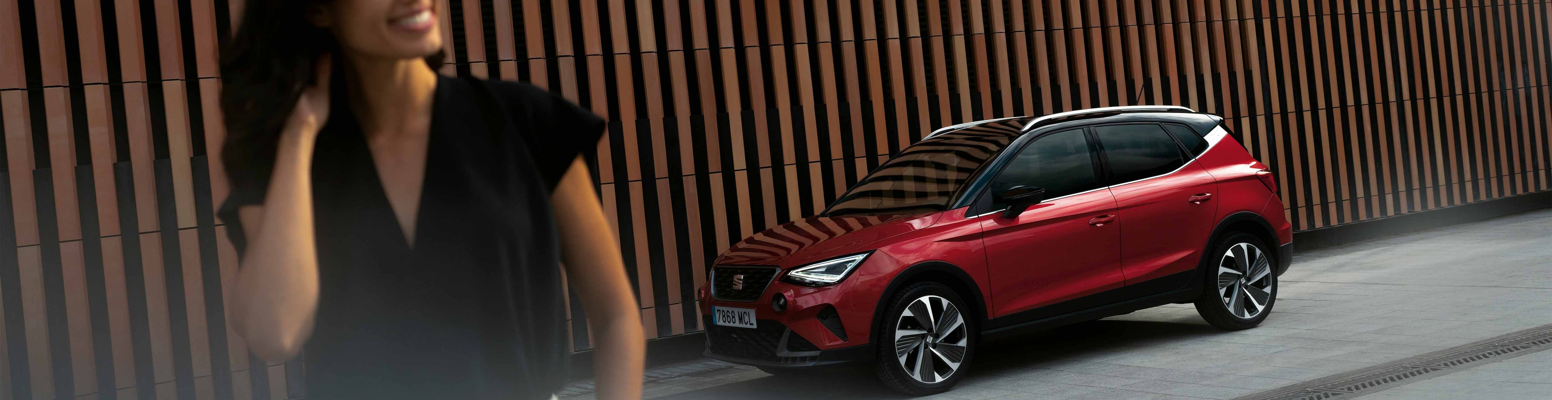 Seat arona in red outside a seat dealership, with wooden panel background, woman in foreground